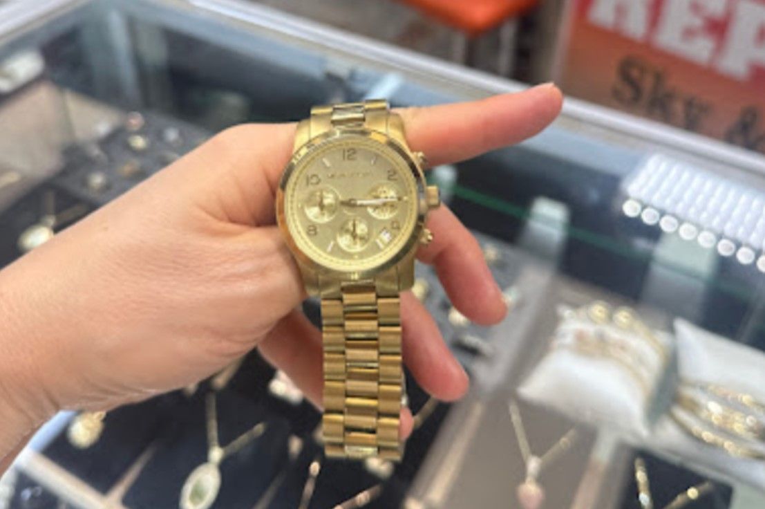 A person holding a gold-tone Michael Kors watch